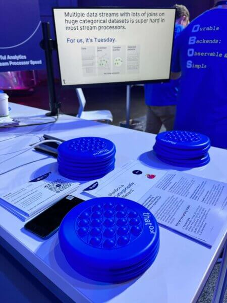 hatDot booth at Current conference showing blue frisbees, a paper stack that says, "thatDot is Categorically different," and a screen that says, "Multiple data streams with lots of joins on huge categorical datasets is super hard in most stream processors. For us, it's Tuesday."